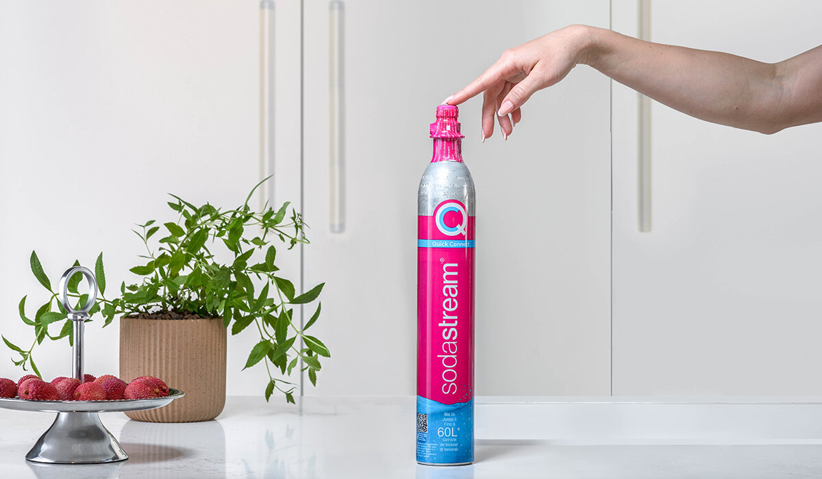 Cylinder SodaStream Quick Connect różowy widok od frontu na rękę dotykającą nabój