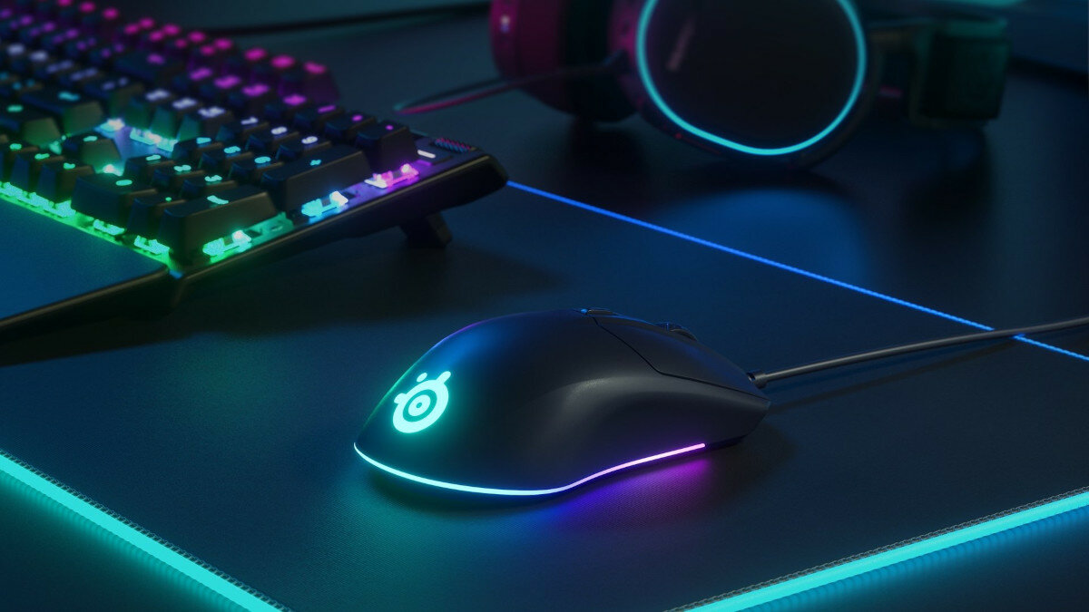 Mysz SteelSeries Rival 3 od boku pokazana wraz z klawiaturą na podkładce SteelSeries