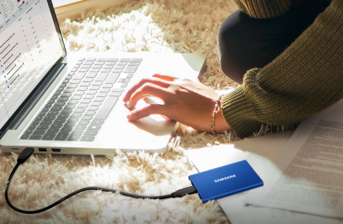 Dysk Samsung Portable SSD T7 podłączony do laptopa który znajduje się na dywanie