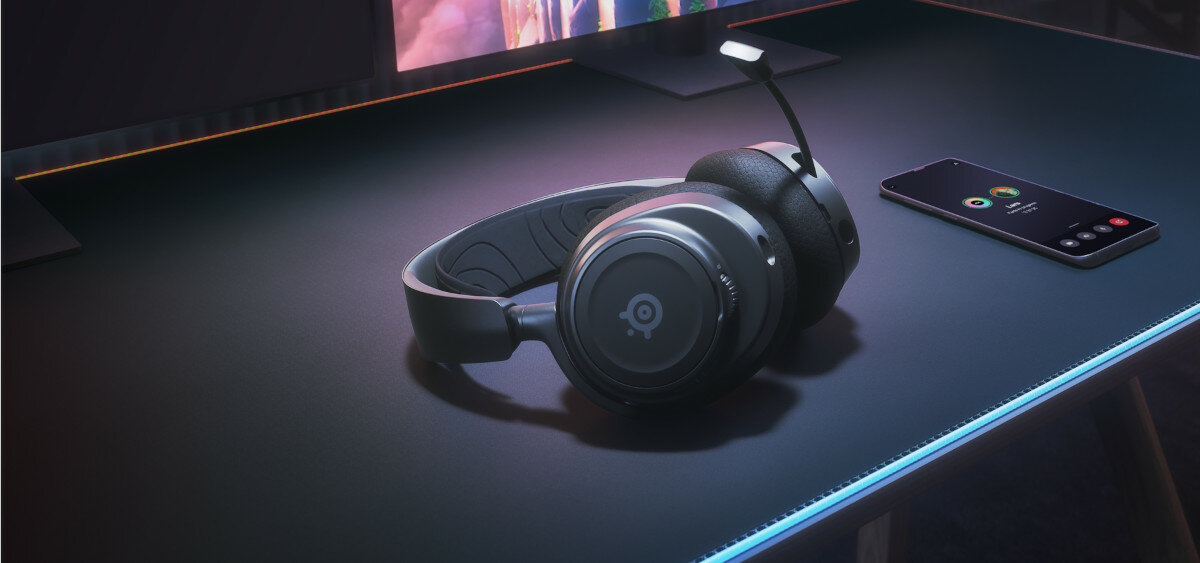 Słuchawki SteelSeries Arctis Nova 7 na blacie biurka wraz z telefonem