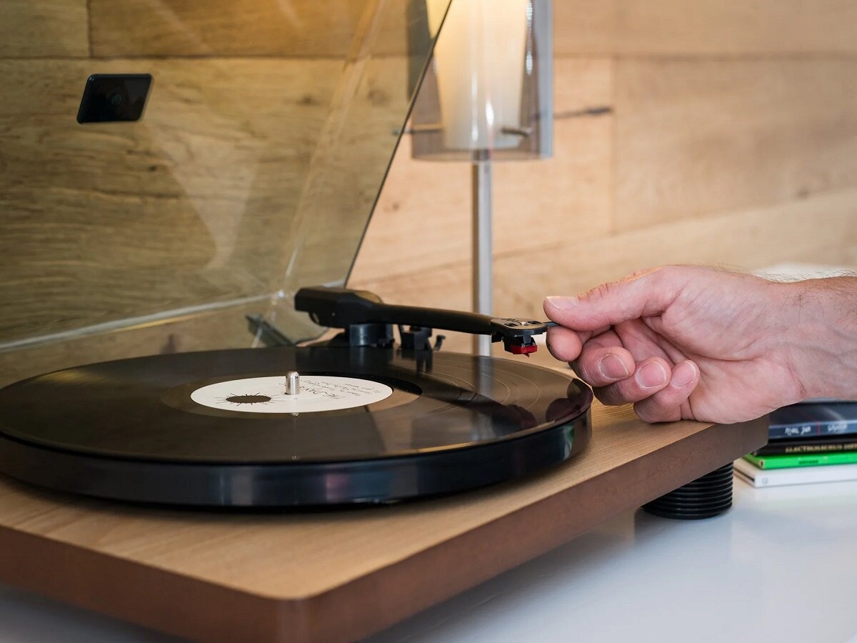 Gramofon Lenco LS-50 WD 50-60 Hz na stole w pokoju z ręką ustawiającą igłę