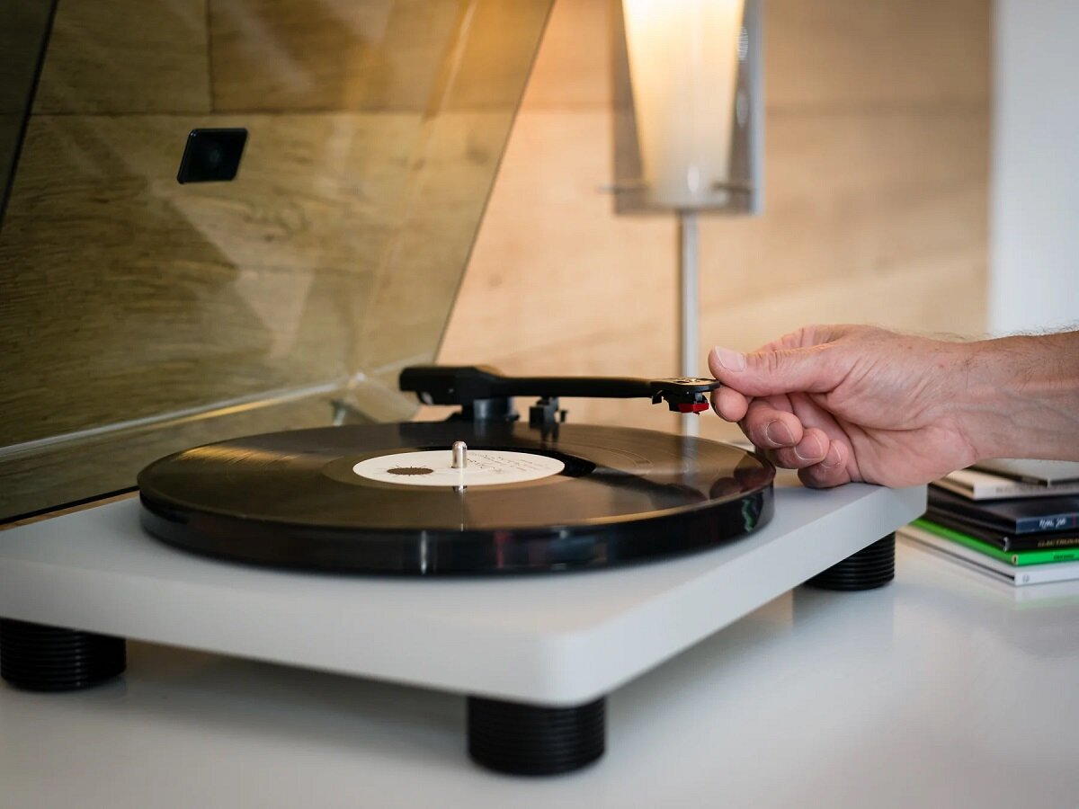 Gramofon Lenco LS-50 GY Szary na stoliku w pokoju z mężczyzną opuszczającym igłę na płytę