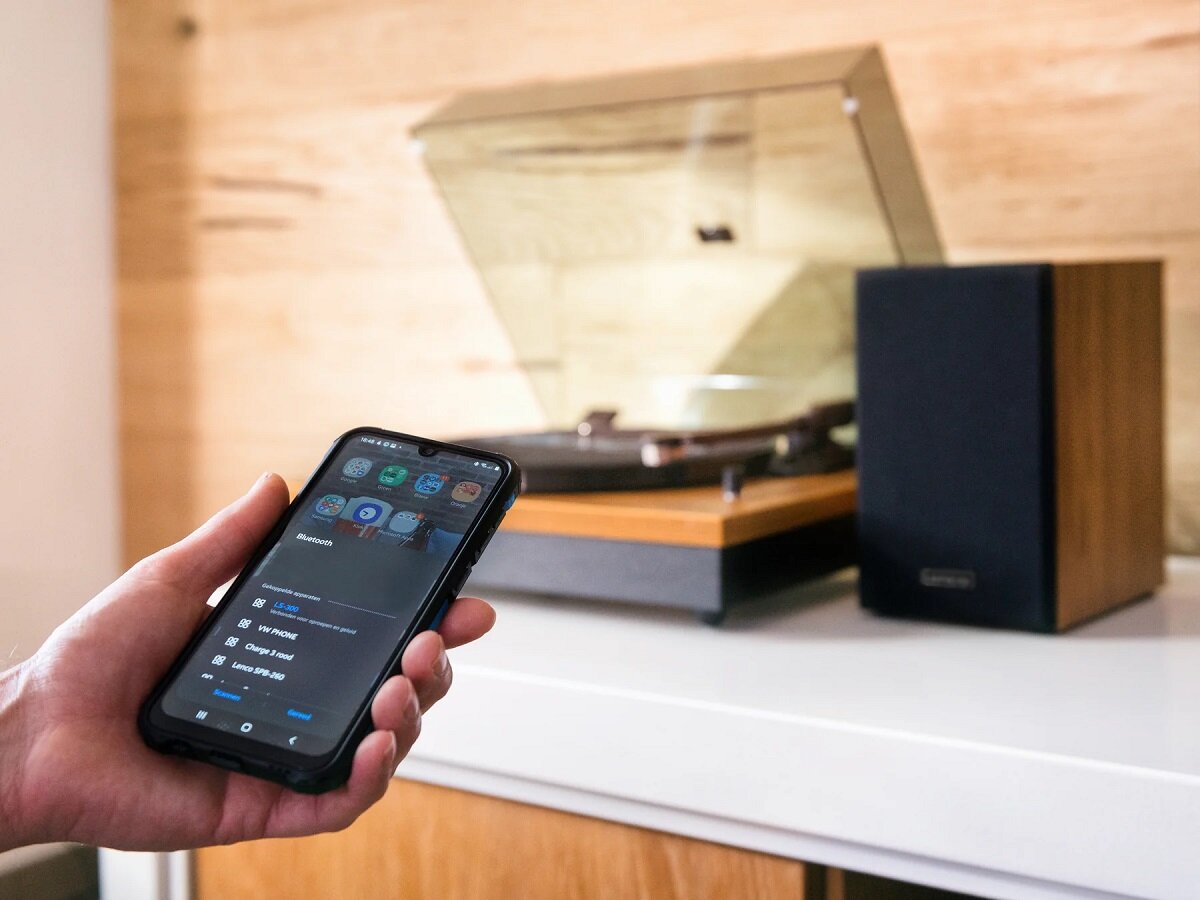 Gramofon Lenco LS-300WD na stole w pokoju z telefonem streamującym muzykę przez Bluetooth
