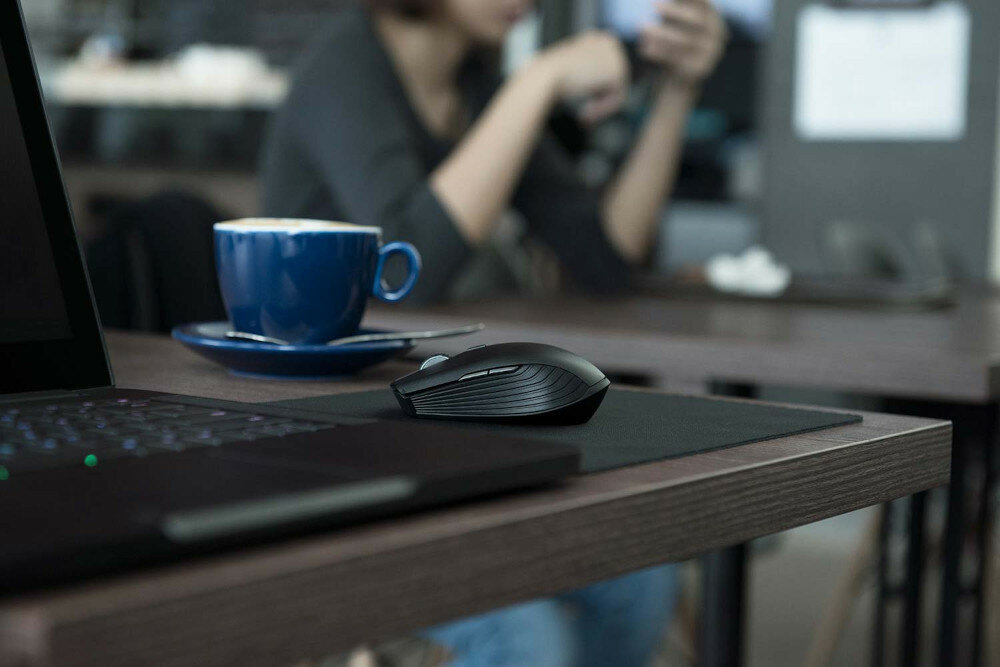 Mysz Razer Atheris - Czarny mysz na podkładce po prawej stronie laptopa, niebieska filiżanka z tyłu