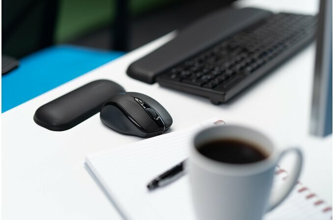 Podkładka pod nadgarstki Kensington ErgoSoft czarna grafika przedstawia podkładkę oraz myszkę na biurku przed nimi kubek na zeszycie z długopisem w tle klawiatura z podkładką