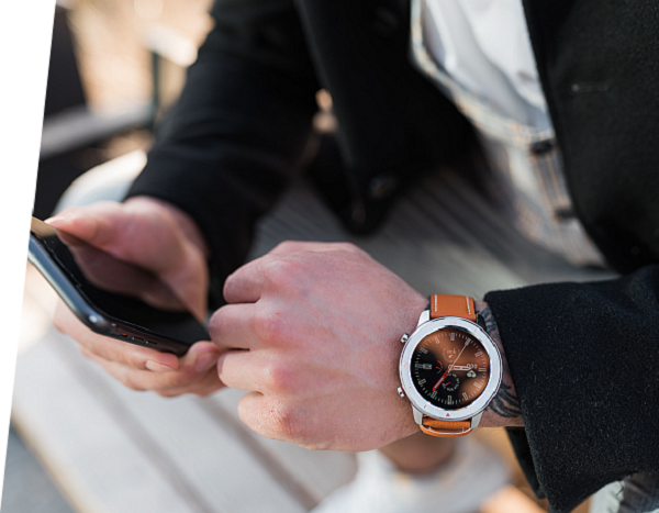 Smartwatch Garett Men 5S brązowy na ręce mężczyzny, obok telefon w dłoni