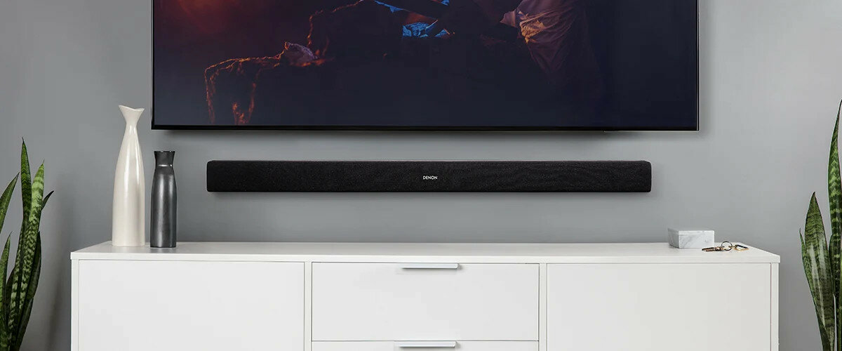 Soundbar Denon DHT-S216 czarny zawieszony na ścianie pomiędzy szafką i telewizorem