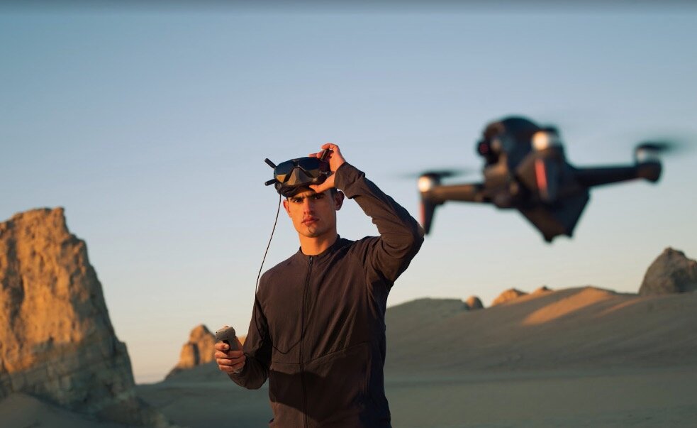 Dron DJI FPV szary widok widok na mężczyznę w goglach sterującego unoszącym się dronem