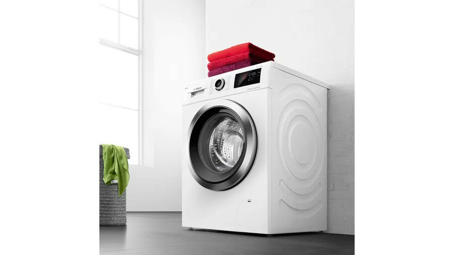 Pralka Bosch WIW28541EU widok na pralkę od dołu pod kątem, pralka w pralni, czerwone ubrania na pralce