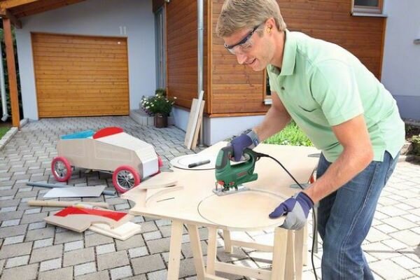 Wyrzynarka Bosch PST 650 urzadzenie podczas pracy na tle domu mężczyzna wyrzyna w drewnie