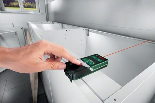 Cyfrowy Dalmierz Laserowy Bosch PLR 50 C urządzenie podczas pracy w scenerii domowej, pomiar szafki