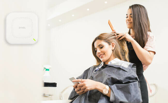 Router Zyxel NWA50AX 802.11ax (Wi-Fi 6) widok na router umieszczony na ścianie w salonie fryzjerskim, gdzie kobieta korzysta z wi-fi na smartfonie
