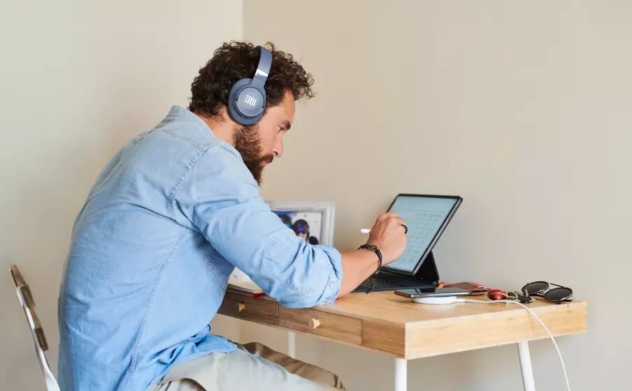 Słuchawki JBL Tune 760NC JBLT760NCWHT widok na mężczyznę przy laptopie ze słuchawkami na uszach