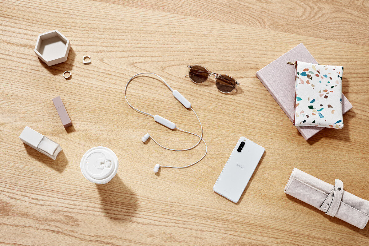 Słuchawki Sony WI-C100W białe pokazane słuchawki położone na stole z innymi rzeczami
