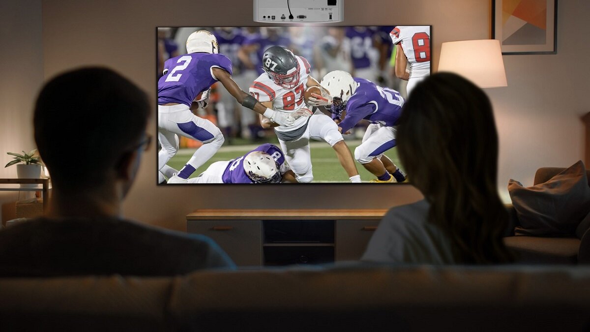 Projektor Optoma UHD35STx UHD wyświetlający mecz futbolu amerykańskiego parze na kanapie