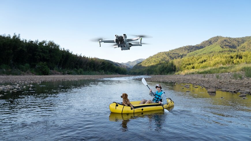 Dron DJI Mini 3 Fly More Combo CP.MA.00000610.01 latający nad wodą oraz mężczyzna z psem płynący na pontonie