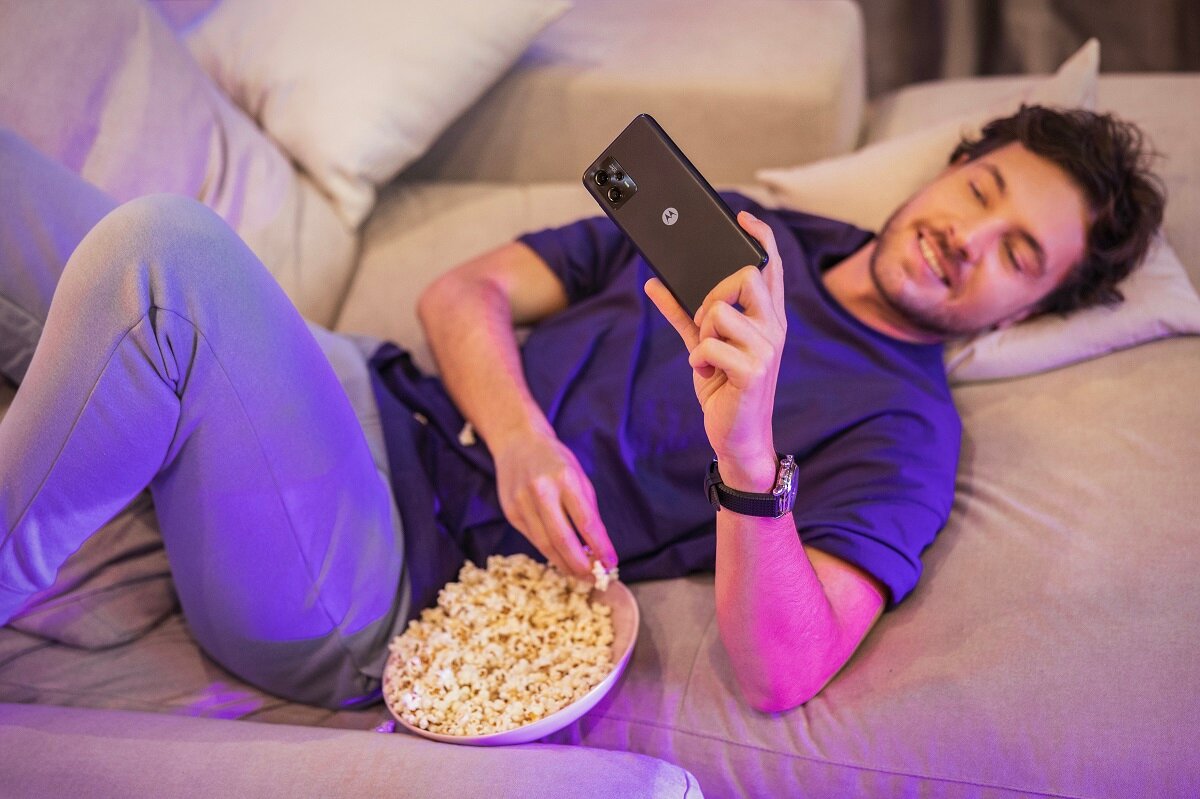 Smartfon Motorola Moto G13 używany przez mężczyznę leżącego na kanapie