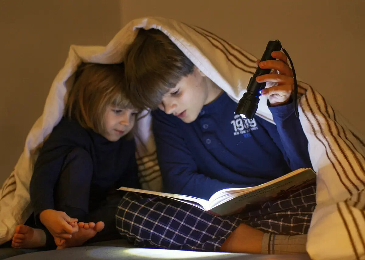 Latarka Extralink EFL-1126 Thor czarna, grafika przedstawia dzieci siedzące pod kołdrą czytające książke którą podświetla chłopczyk latarką