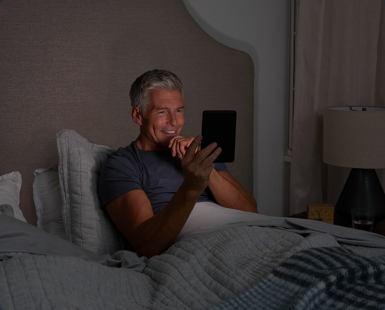 Czytnik e-Booków Amazon Kindle 11 w rękach mężczyzny leżącego na łóżku
