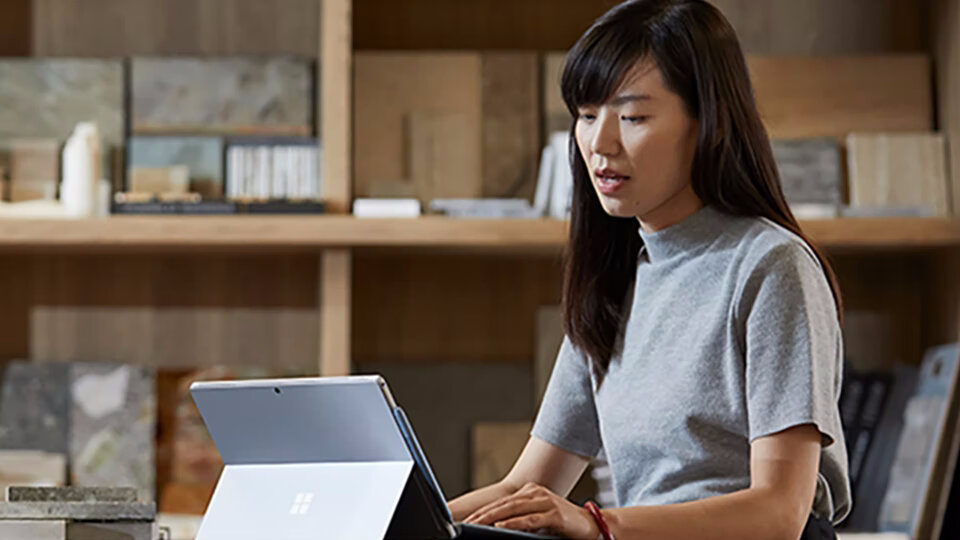 Tablet Microsoft Surface Go 2 4/64GB grafika przedstawiająca kobietę siedzącą przed tabletem w pomieszczeniu, gdzie znajduję się półki z przedmiotami