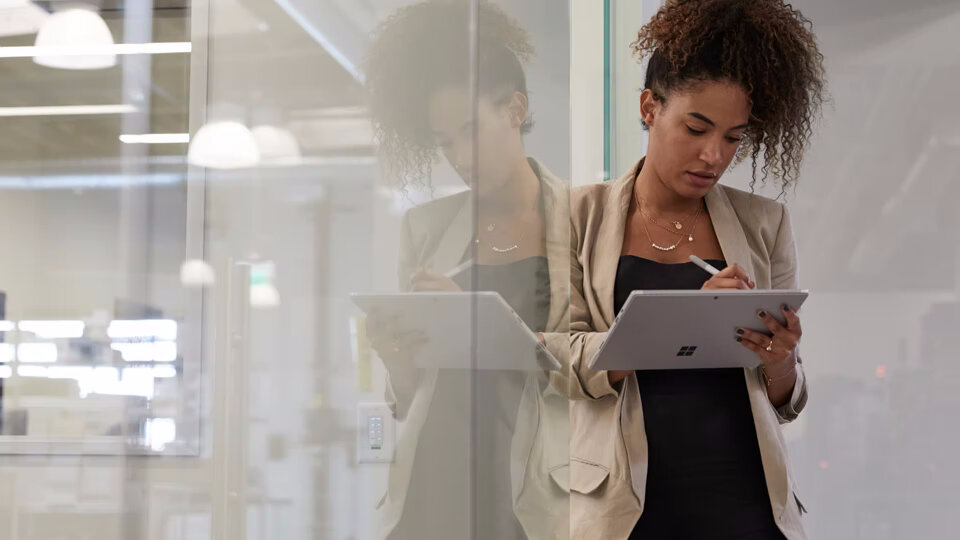 Tablet Microsoft Surface Go 2 4/64GB kobieta stojąca z tabletem i piórem w dłoniach na tle szklanej ściany