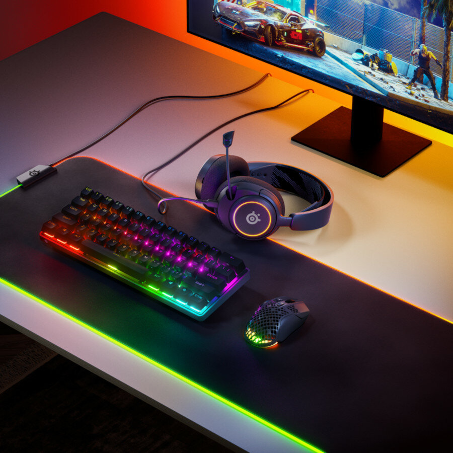 Słuchawki SteelSeries Arctis Nova 3 na blacie biurka wraz z myszką, klawiaturą i podkładką oraz monitorem