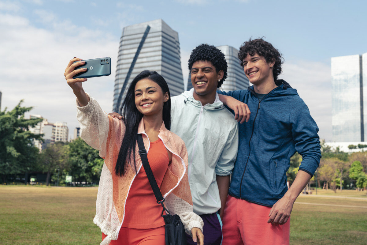 Smartfon Motorola moto g42 4/128GB różowy od tyłu, w ręce kobiety robiącej selfie sobie i przyjaciołom na tle budynków