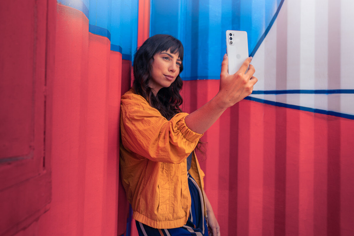 Smartfon Motorola moto g52 od tyłu, w ręce kobiety robiącej sobie selfie na tle kontenera
