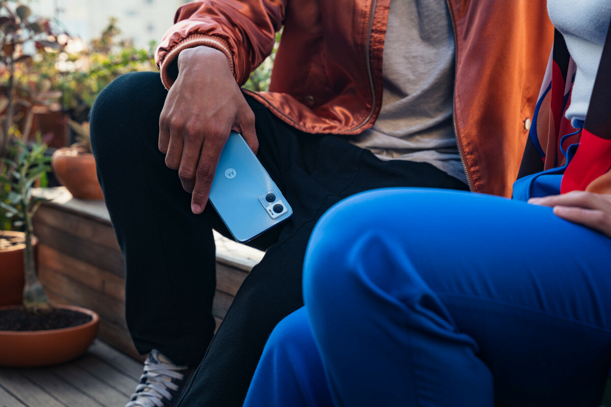 Smartfon Motorola moto e22 od tyłu, w dłoni mężczyzny który siedzi na ławce z drugą osobą