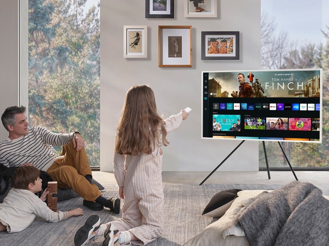 Telewizor Samsung The Frame LS03BG 4K grafika przedstawia rodzinę siedzącą przed telewizorem, korzystającą z funkcji Smart Hub