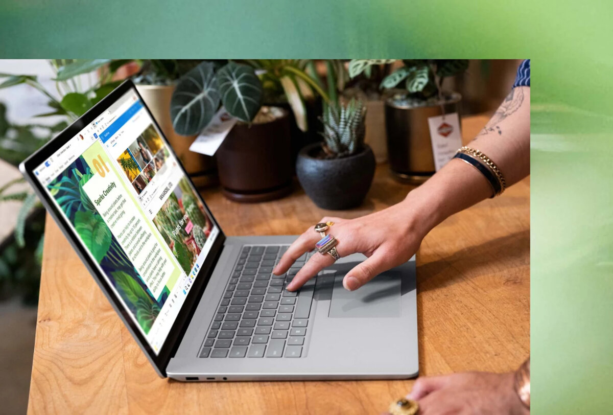 Laptop Microsoft Surface 5 15” platynowy grafika przedstawia ręce kobiety piszące na klawiaturze laptopa stojącego na biurku w tle rośliny w doniczkach