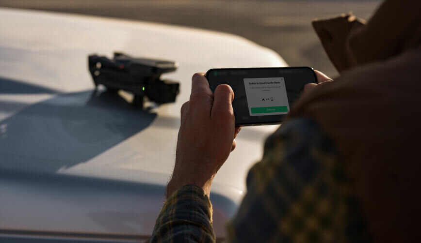Dron DJI Mavic 3 Pro Cine Premium Combo widok na złożonego drona w tle i trzymany w dłoniach telefon w pozycji poziomej