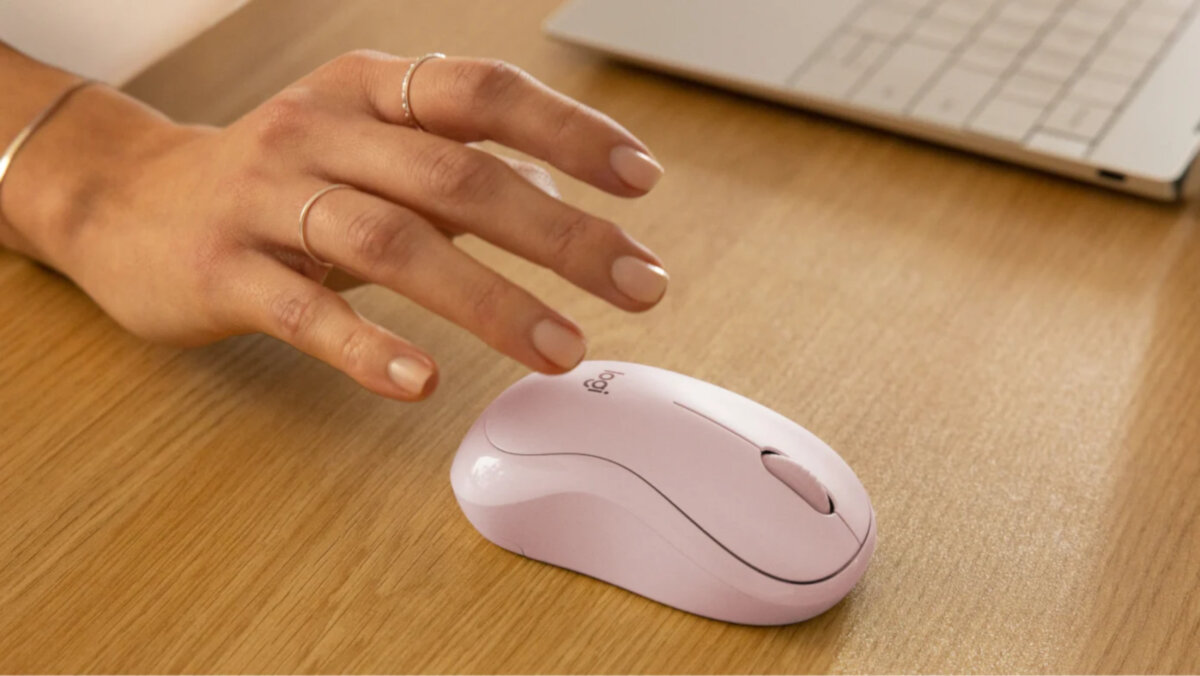 Mysz Logitech M240 Silent różowa grafika przedstawia mysz leżącą na biurku nad nią ręka kobiety obok laptop