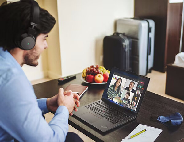 Laptop Lenovo ThinkPad X13 G4 16GB/1TB grafika przedstawiająca męzczyznę w słuchawkach siedzącego przed włączonym laptopem, obok notatniki z długopisami, maska, owoce na talerzu oraz pilot, w tle walizki koło szafki