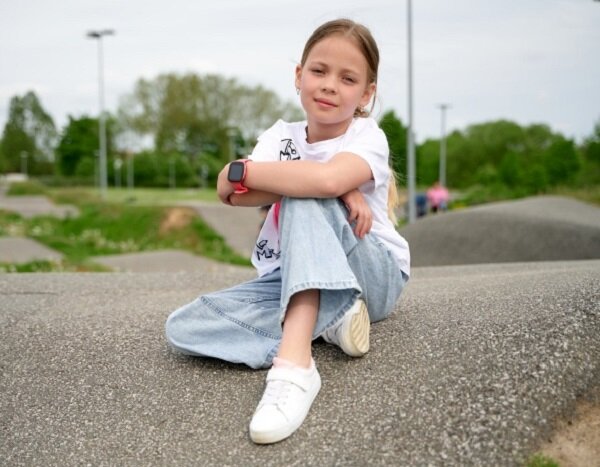 Smartwatch Garett Kids FIT dziewczynka siedząca na ulicy z zegarkiem na ręku