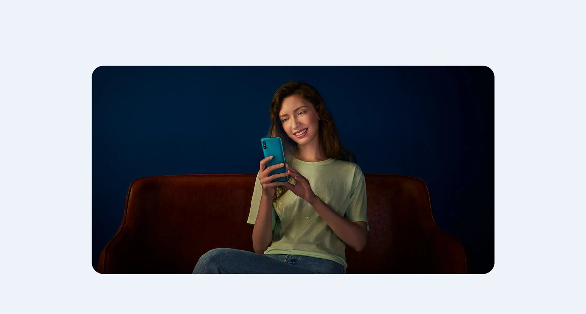 Smartfon Xiaomi Redmi 9A 2/32GB szary kobieta siedząca w ciemnym pokoju na sofie ze smartfonem w rękach