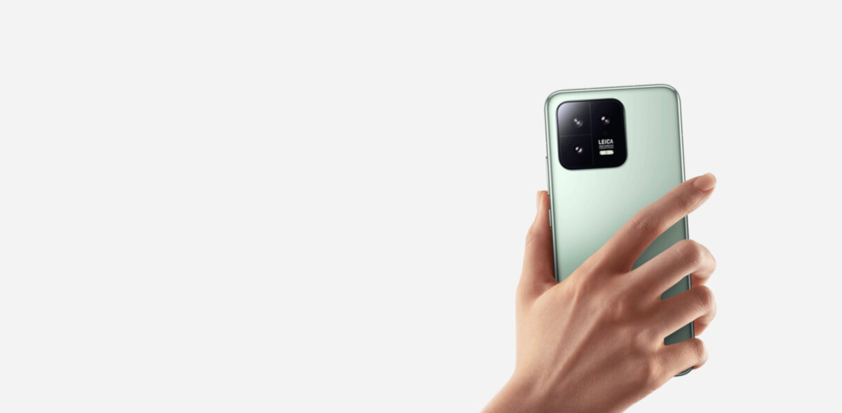 Smartfon Xiaomi 13 8/256 GB czarny grafika przedstawiająca rękę trzymającą smartfon tyłem z widocznym aparatem na białym tle