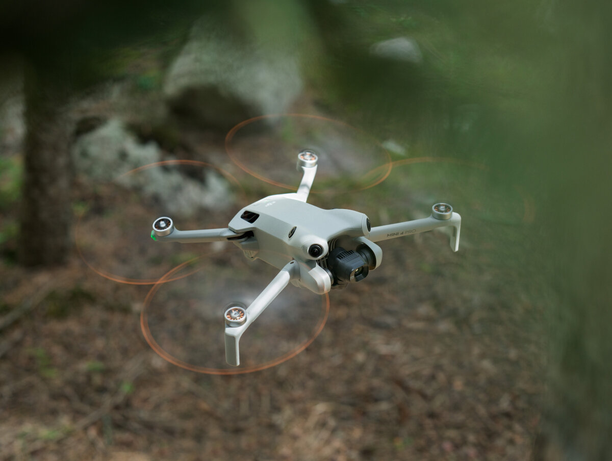 Dron DJI Mini 4 Pro Fly More Combo (DJI RC 2) grafika przedstawiająca dron od góry unoszący się nad ziemią w lesie