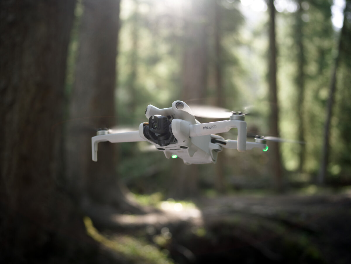Dron DJI Mini 4 Pro (RC-N2) grafika przedstawiająca dron po skosie unoszący się nad ziemią w lesie