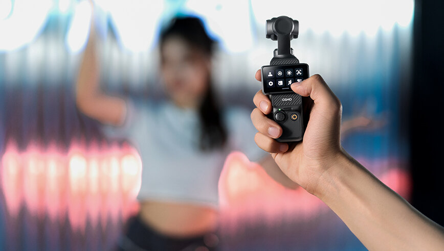 Kamera DJI Osmo Pocket 3 widok na grafikę przedstawiającą kamerę trzymaną w dłoni na rozmytym tle z widoczną na nim kobietą