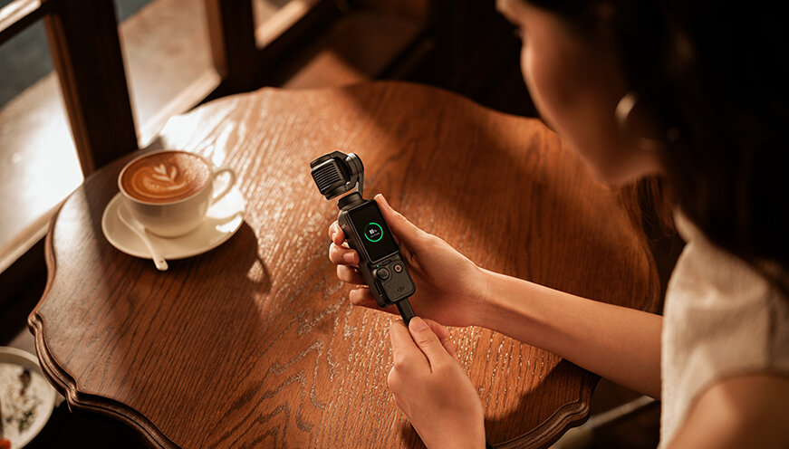 Kamera DJI Osmo Pocket 3 widok na kamerę pod skosem trzymaną w dłoni z widocznym na ekranie stanem naładowania baterii