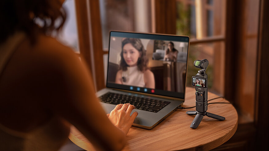 Kamera DJI Osmo Pocket 3 Creator Combo widok na laptopa i kamerę na stoliku oraz na kobietę patrzącą na ekran laptopa w trakcie rozmowy wideo