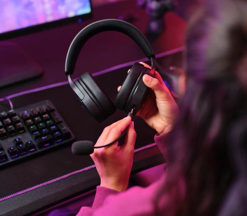 Słuchawki Trust GXT489 Fayzo czarny grafika przedstawia kobietę która montuje do słuchawek mikrofon w tle monitor i klawiatura