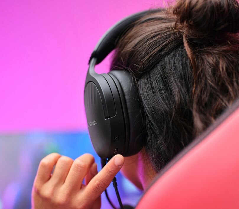 Słuchawki Trust GXT489 Fayzo czarny grafika przedstawia kobietę ustawiająca głośność na słuchawkach które na na uszach
