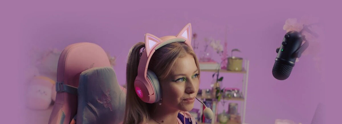 Słuchawki Razer Kraken Kitty V2 różowe grafika przedstawia kobietę siedzącą w słuchawkach przed mikrofonem