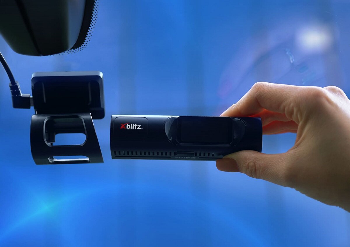 Wideorejestrator Xblitz V4 Professional 2.5K grafika przedstawia rękę wkładającą widerejestrator do uchwytu w samochodzie